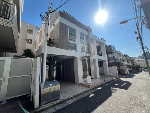 日差しが強い晴れた日に撮影された都市のアパート外観、現代的な建築スタイル、歩道と街路灯が見える