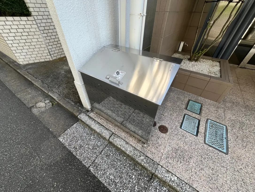 都市の歩道に設置されたステンレス製のごみ箱、白いタイルの壁、マンホールと排水溝の蓋