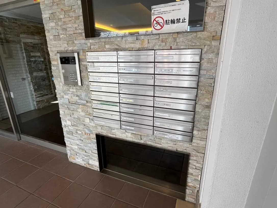 マンションのエントランスにある宅配ボックスとインターフォン、石積みの壁装飾と禁煙のサイン