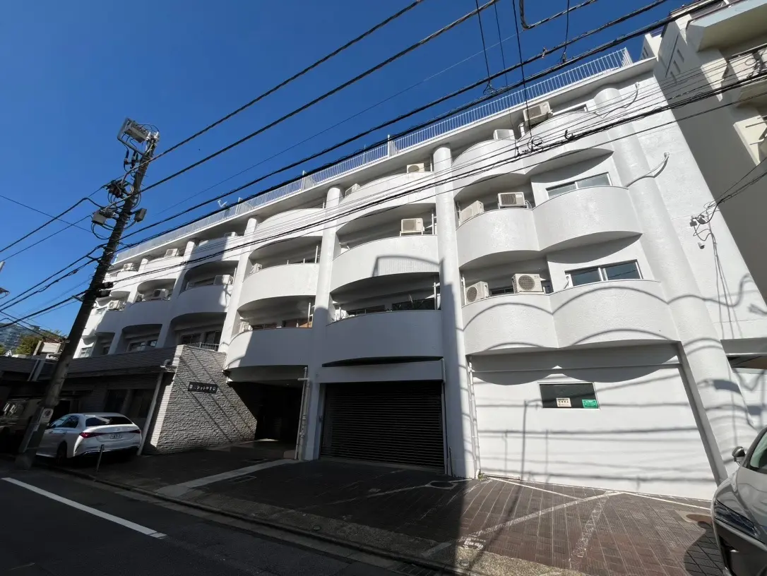 白い外壁のモダンなアパート建築、バルコニー付き、晴れた日の青空と影が映える外観