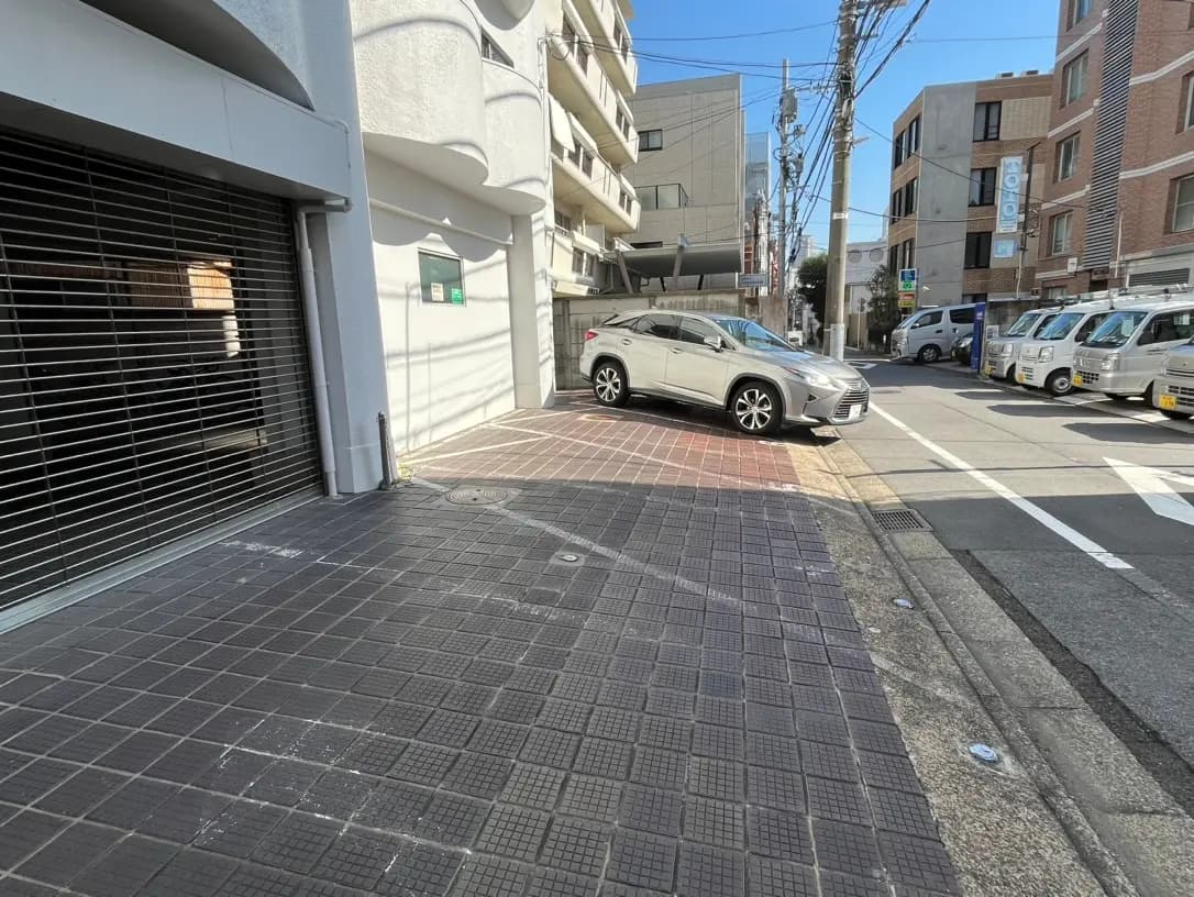 都市の路上に駐車されたシルバーのSUV、マンションと電柱、晴れた日の市街地風景