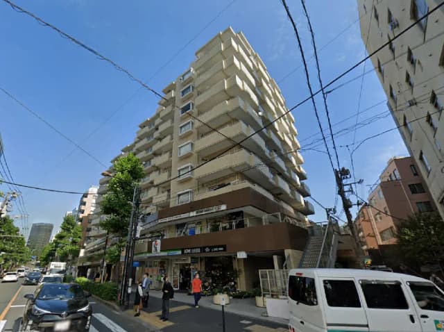 - 都市の商業エリアに位置する現代的な高層マンションの外観、青空と電線が背景に広がる風景