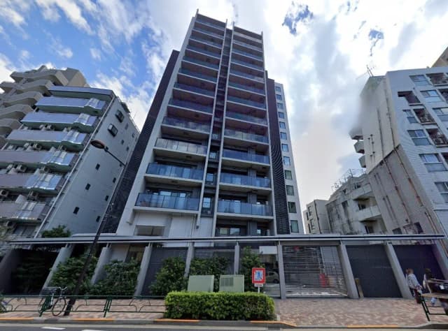 - 高層マンションの外観、バルコニーのあるモダンなデザイン、周囲の建物と青空が広がる風景