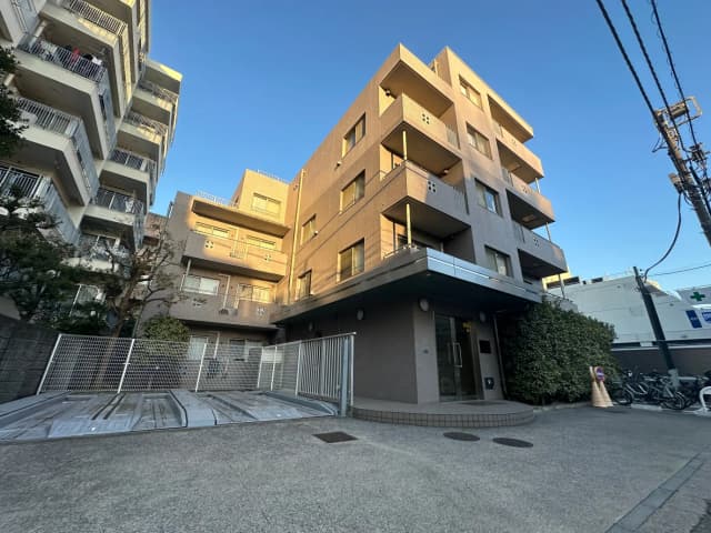 日の光が当たる近代的なマンション外観、駐輪場あり、青空に映える建物フェイサード