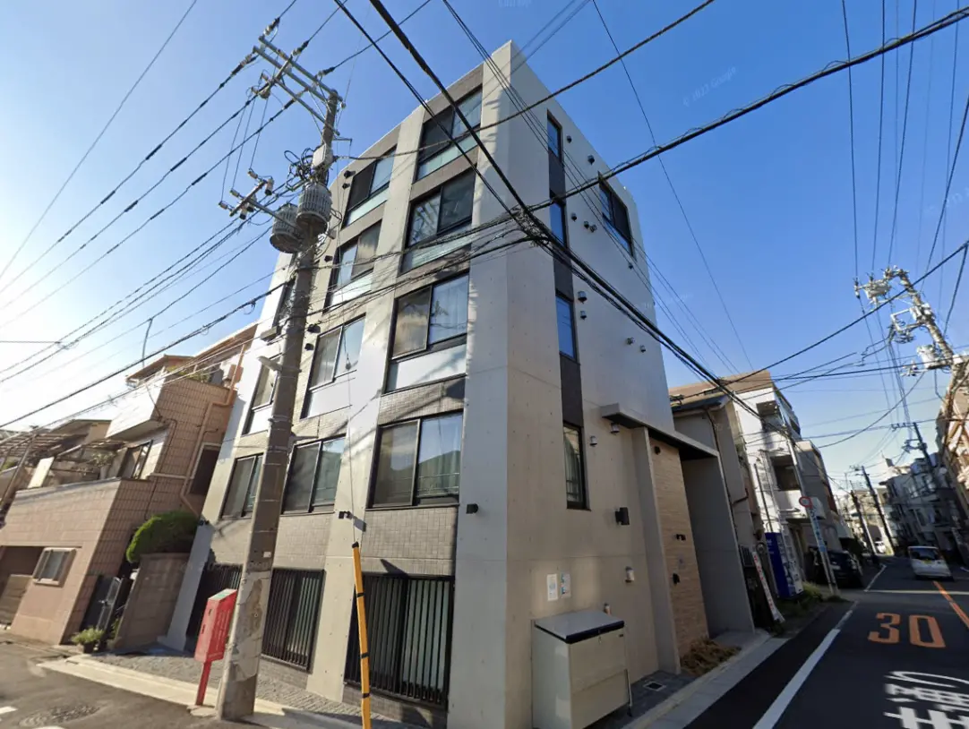 - モダンな外観の集合住宅、周囲に電柱と電線が見える、晴れた青空の下で撮影された写真