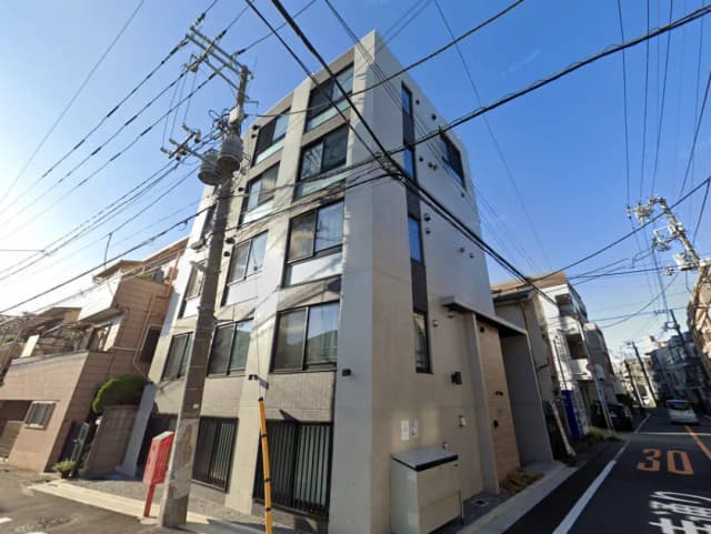 - モダンな外観の集合住宅、周囲に電柱と電線が見える、晴れた青空の下で撮影された写真