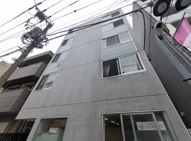 - コンクリート造の現代的な外観のビル、上部に大きな窓があり、周囲に電柱と電線がある街中の風景