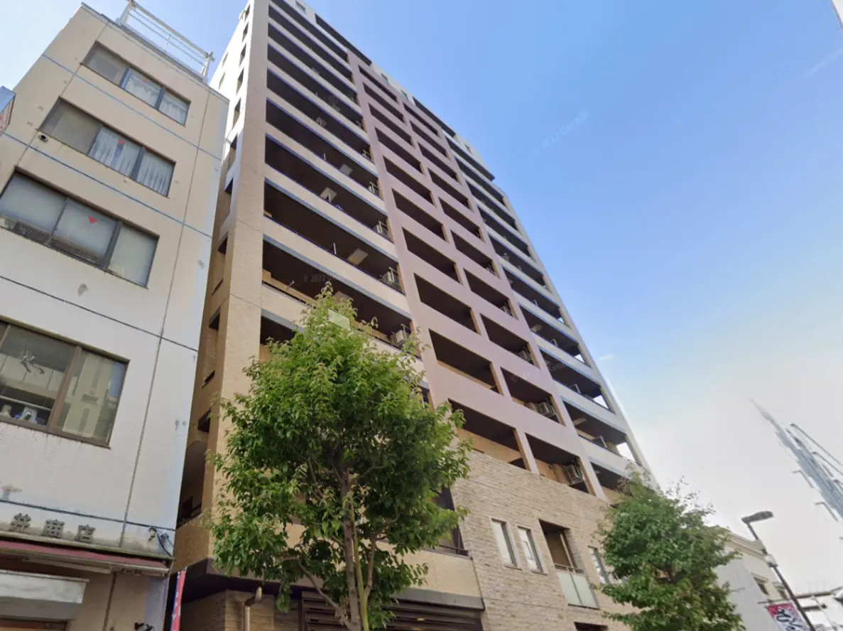 - 現代的なデザインのマンション、周囲にある建物や木々が映えるエクステリア、青空を背景にした外観の写真