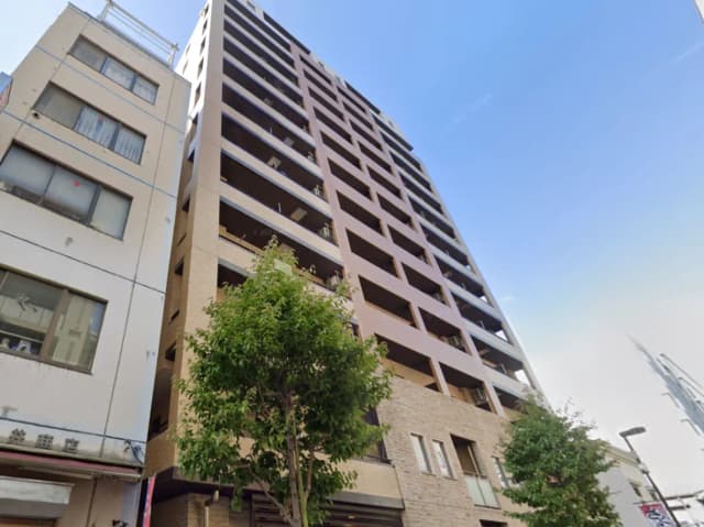 - 現代的なデザインのマンション、周囲にある建物や木々が映えるエクステリア、青空を背景にした外観の写真