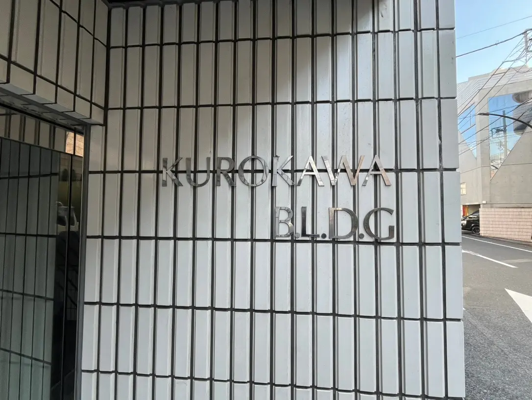 建物の壁面に取り付けられた「KUROKAWA BLDG」と表示された看板、都市の建築と縦線のデザイン