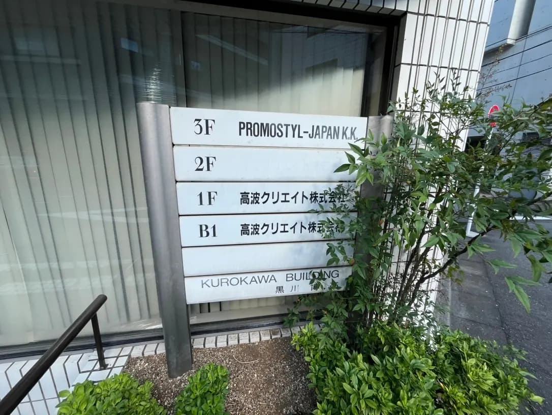 ビルの入口案内板、階数表示とテナント名、植栽付きの外観