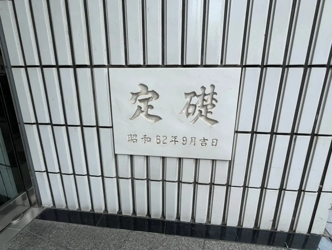 建物の壁に取り付けられた「大崎」の表示看板、白いタイルデザインの壁面