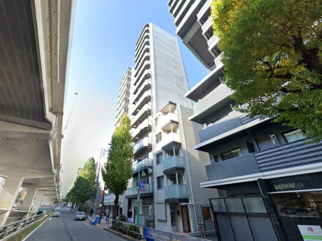 日差しが降り注ぐ都市の道路沿いに建つモダンなマンションとビル、緑豊かな街路樹