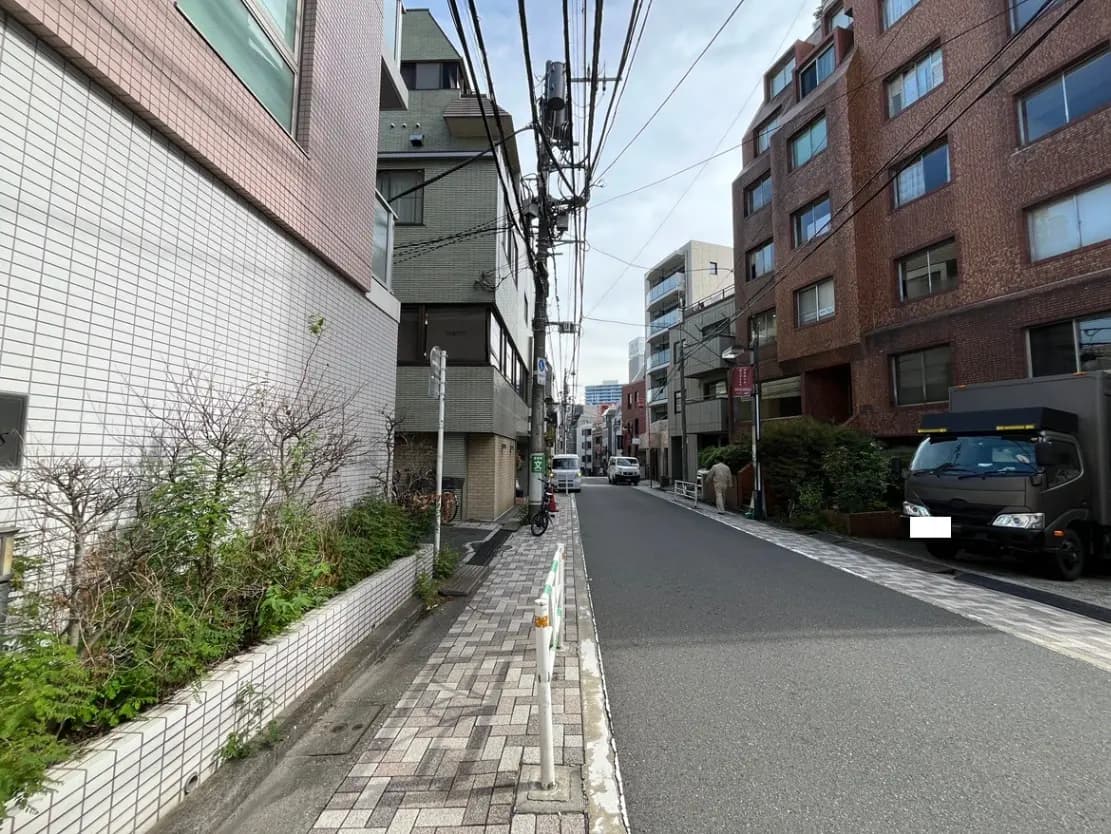 - 都市の住宅街にある静かな通り、左右に並ぶレンガ造りの建物と植栽、電柱と電線が目立つ風景