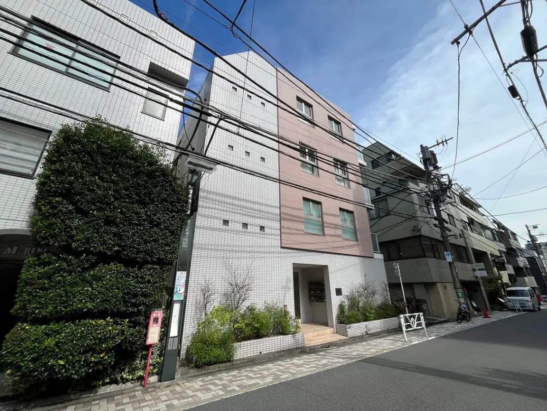 - 白いタイルとピンクの外壁が特徴のマンション、周囲に緑豊かな植栽と電線が通る街並みの風景