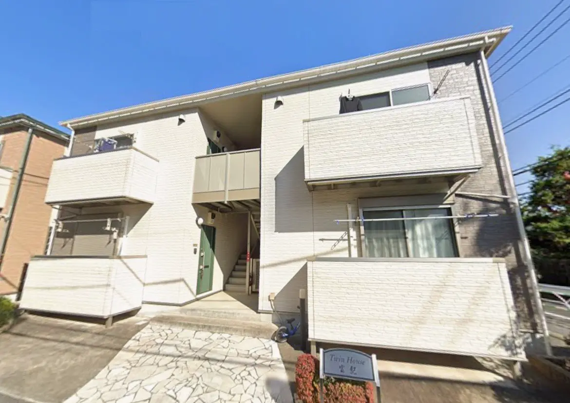 日差しが明るい住宅街に位置するモダンな2階建てのアパート、ホワイトの外壁とバルコニー