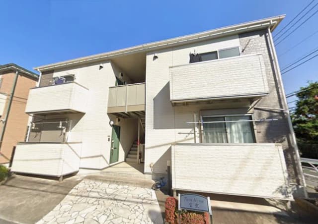 日差しが明るい住宅街に位置するモダンな2階建てのアパート、ホワイトの外壁とバルコニー