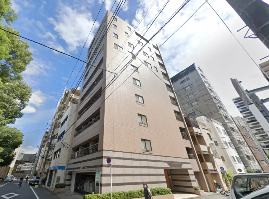 - 都市部に位置するモダンなデザインのマンション、周囲に高層ビルが立ち並ぶ風景と青空のコントラスト