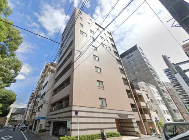 - 都市部に位置するモダンなデザインのマンション、周囲に高層ビルが立ち並ぶ風景と青空のコントラスト