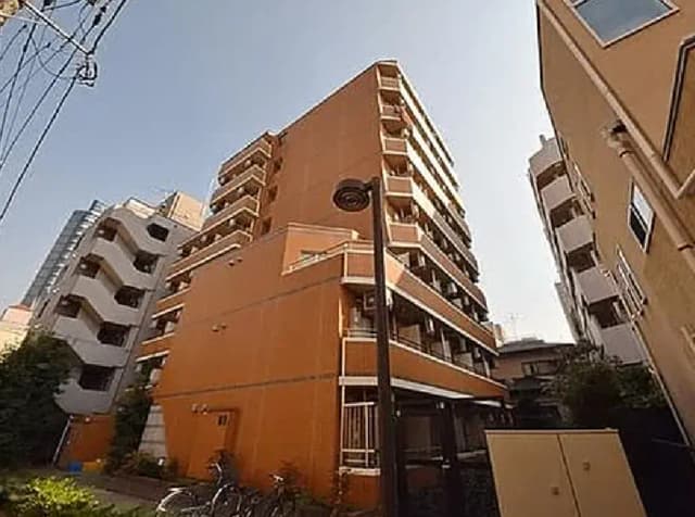 - 明るいオレンジ色の外観を持つ集合住宅、周囲には高層ビルが立ち並び、青空が広がる風景