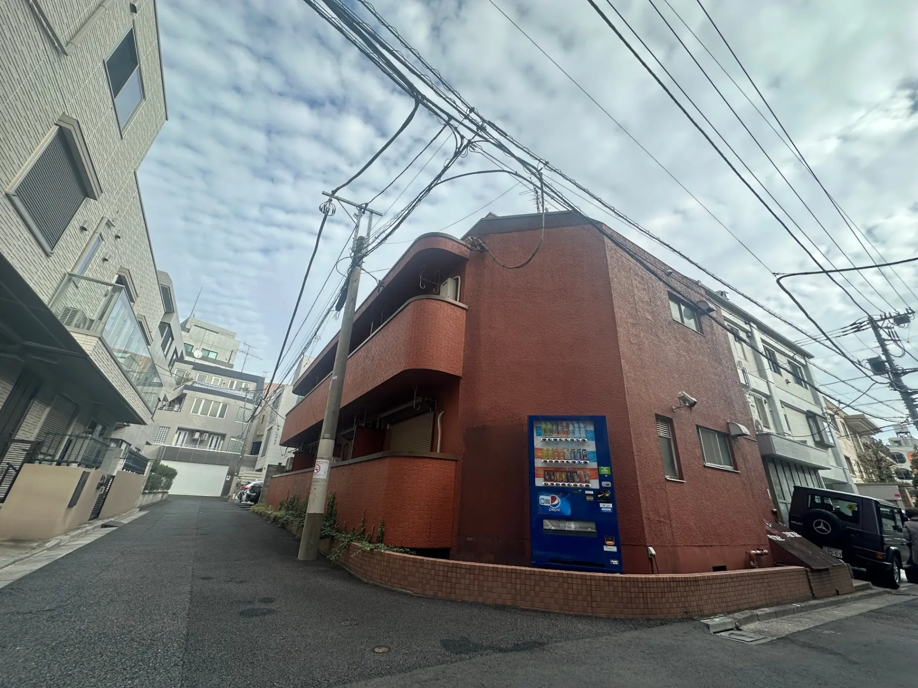 都市の角にあるコンクリート製の建物と通り、交錯する電線、晴れた日の空
