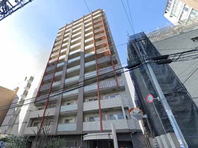 - 都市部に建つ高層マンションの外観、バルコニー付きの部屋と隣接する建物、青空が広がる背景