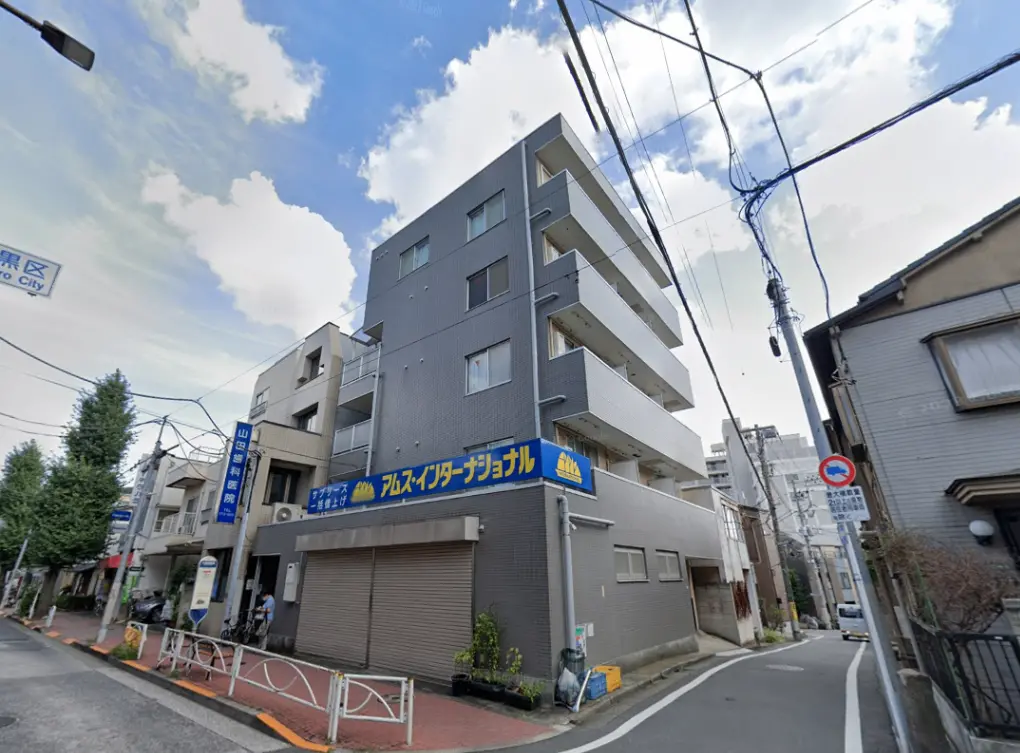 - 都市部に位置する現代的なアパートメントビル、青い看板と周囲の住宅街が広がる風景