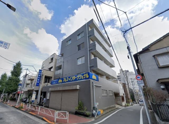 - 都市部に位置する現代的なアパートメントビル、青い看板と周囲の住宅街が広がる風景