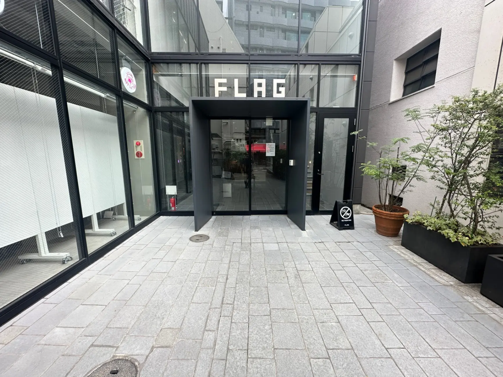 モダンな建築スタイルの入り口、ガラス扉と「FLAG」と表示されたサイン、都会的な雰囲気の外観デザイン