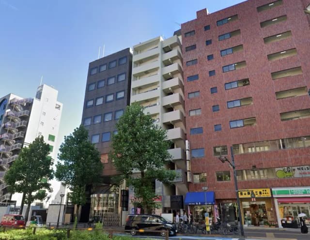 - 都市のビル群、黒い外壁の建物と赤いレンガ調のビル、周囲に植えられた大きな樹木がある通りの風景