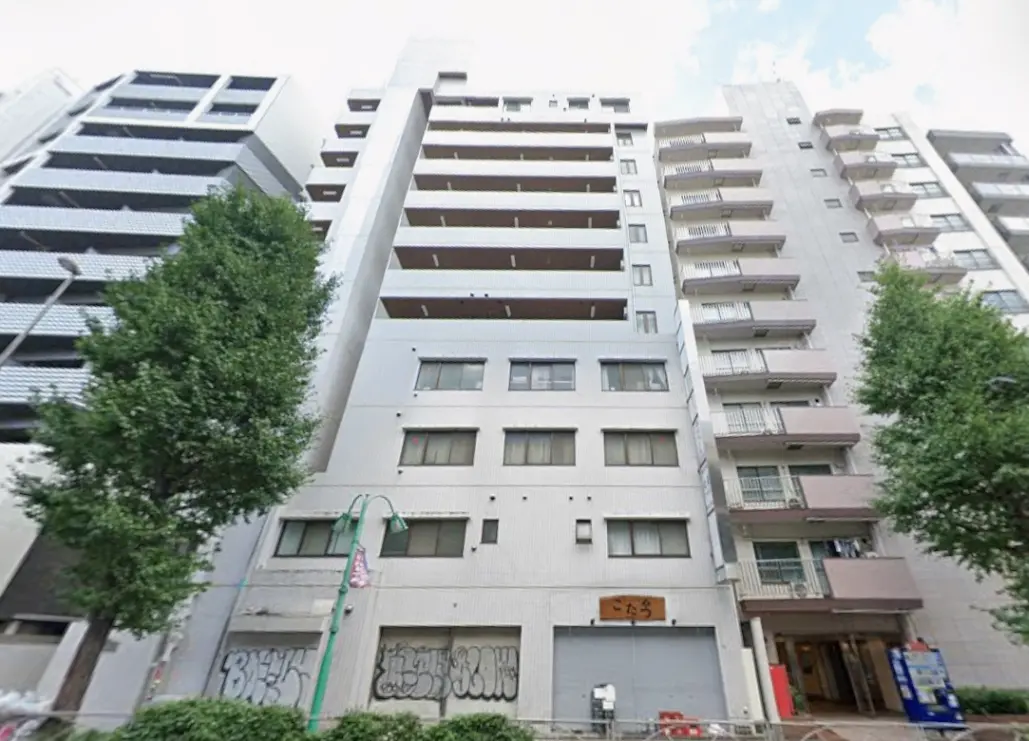 - 都市型マンションの外観、モダンなデザインと緑豊かな街路樹が共存する風景