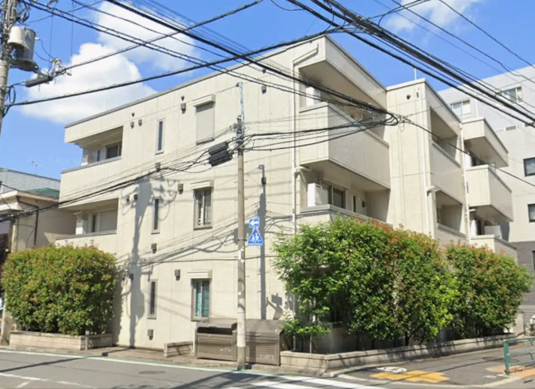 - シンプルでモダンなデザインの集合住宅、周囲には緑の植栽と電線が交差する通りの風景