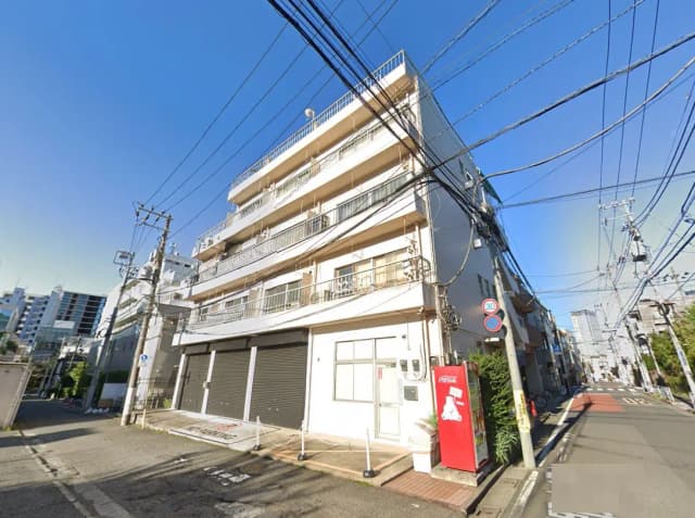 - 都市のアパートメントビル、商業施設の近くに位置し、街路に面したエントランスと自動販売機がある様子