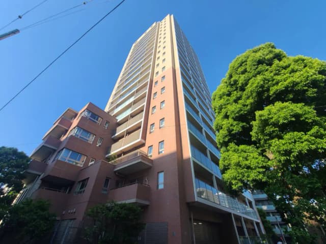 高層マンションの外観、青空の下にそびえ立つモダンなデザインと周囲の緑の木々