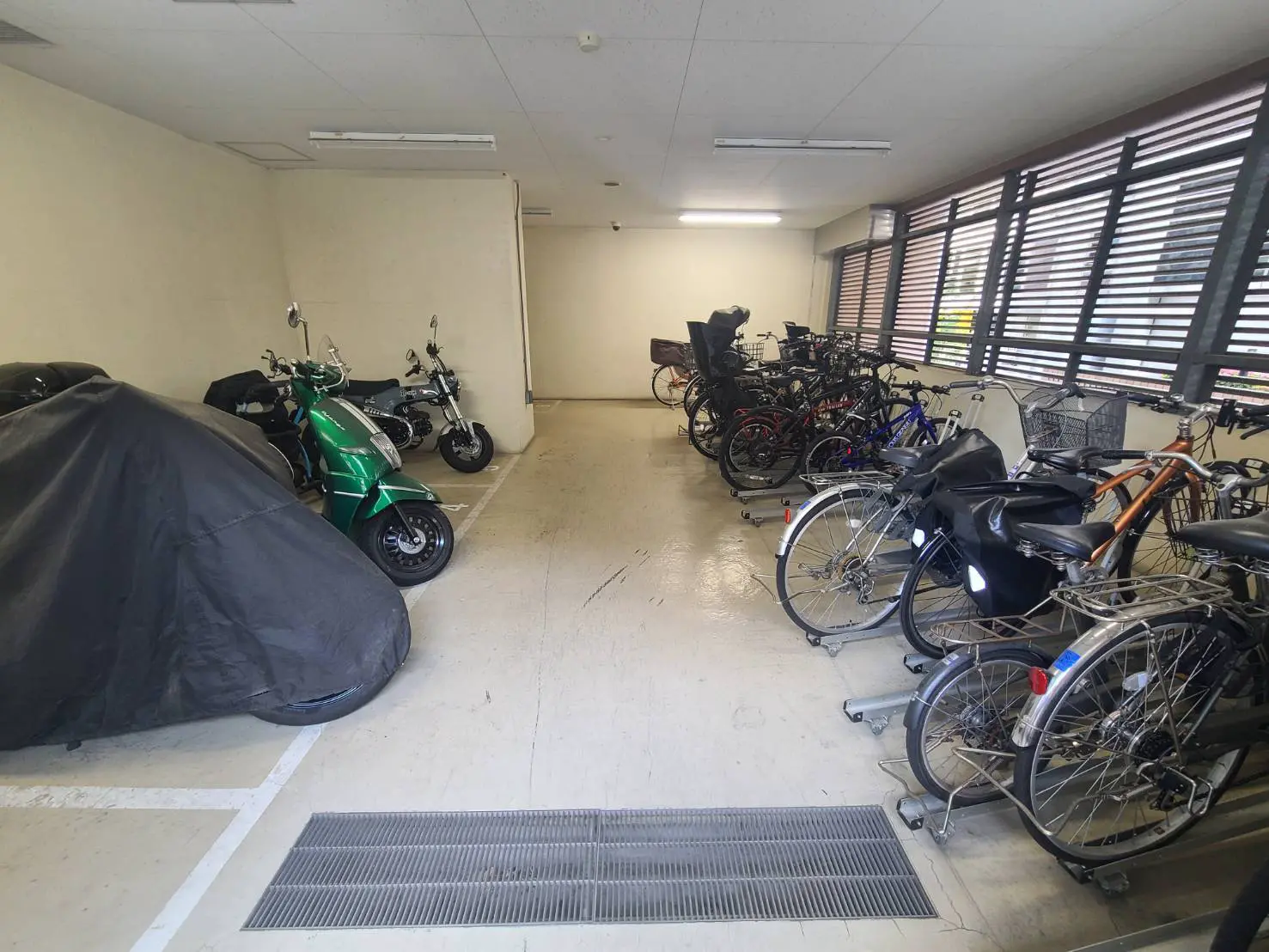 - バイクと自転車が並ぶ屋内駐輪場、黒いカバーがかけられたバイク、明るい照明の中に整然と配置された自転車