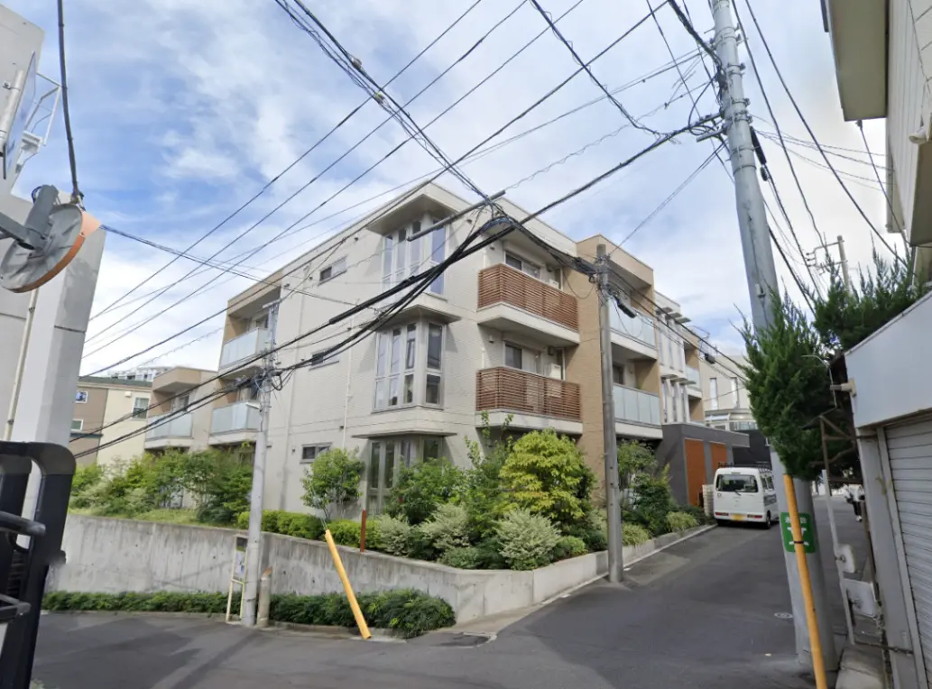 - 住宅街にあるモダンなアパートメントビル、周囲には緑豊かな植栽と電柱が立ち並ぶ風景
