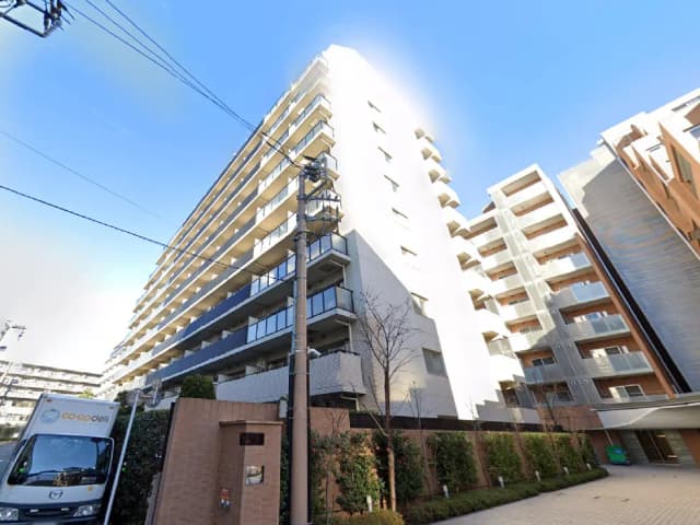 - 現代的なデザインのマンション外観、青空を背景にした複数階建ての建物と緑豊かなエントランス付きの住宅街の風景