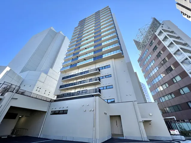 - 高層マンションの外観、青空を背景にしっかりとしたデザインのエントランスとバルコニーが特徴の建物