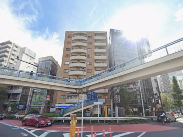 - 都市の交差点にあるマンションの外観、歩道橋が交差している景色と青空の下のビル群