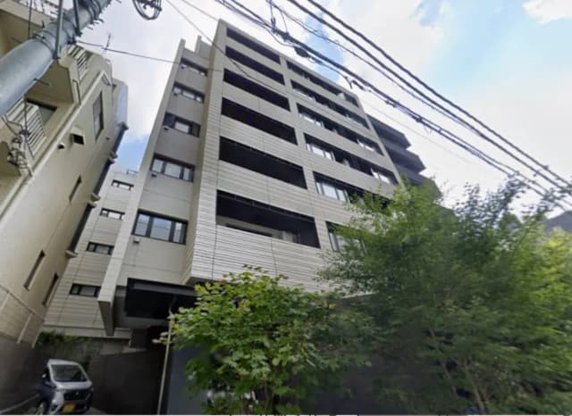 現代的なデザインの4階建てアパートメントビル、隣接する建物と緑の木々が見える様子