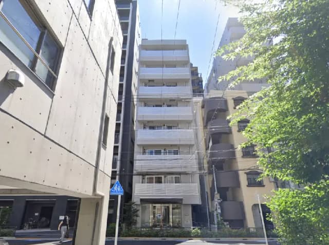 - モダンなデザインのアパートメントビルの外観、周囲には高い建物や緑豊かな植栽がある都市の風景
