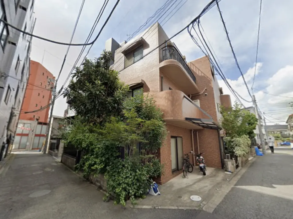 - モダンなデザインの住宅、赤レンガの外壁と緑豊かな植栽、近隣の建物と道路が映る街並み