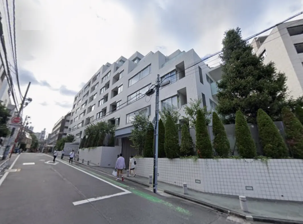 - 近代的なデザインのマンション外観、周囲に緑の植栽が施され、通りに歩行者がいる様子