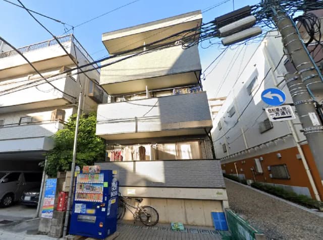 - モダンな外観のアパートメントビル、手前には自動販売機と自転車、青空を背景にした街並みの様子