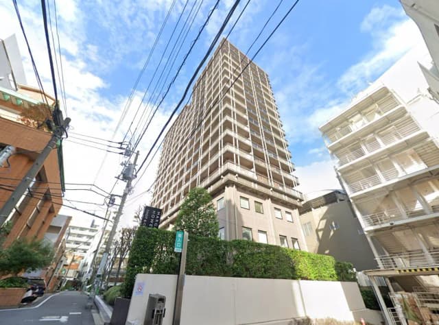 日本の繁華街に立つ現代的な高層マンション、晴れた日の青空と街路樹