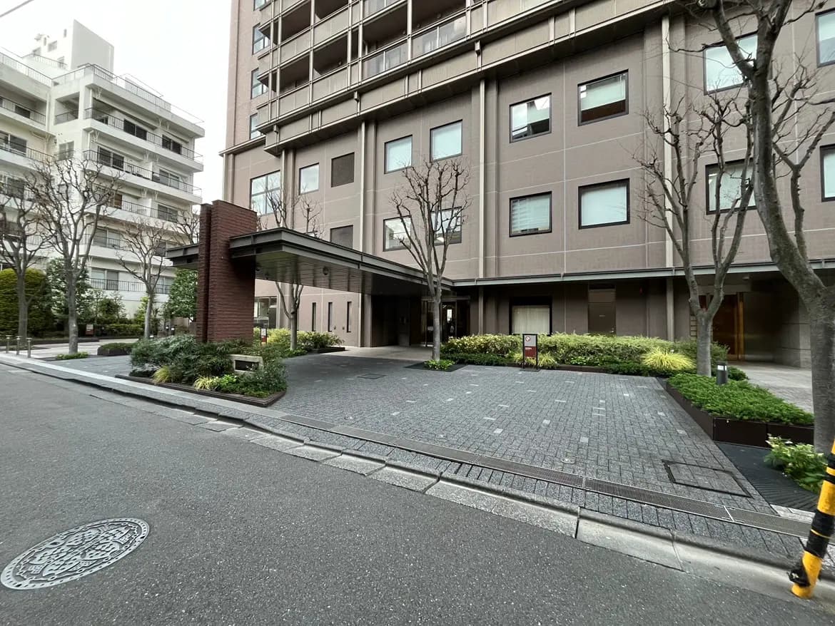 - 現代的なマンションのエントランス、整った植栽と石畳のアプローチ、晴れた日の外観