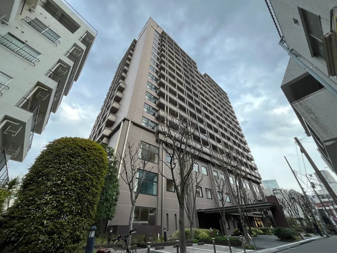 - 現代的なデザインの高層マンション、周囲には緑の植栽と整備された歩道、曇り空の下での立体的な建物の風景