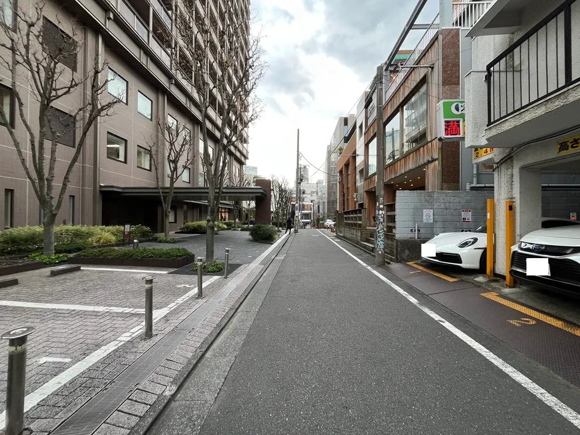 - 都市の静かな通り、両側に並ぶ高層ビルと駐車スペース、乾いた季節の木々が見える風景
