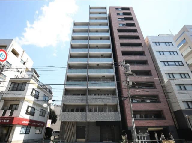 - 都市型のモダンなマンション外観、バルコニー付きのフロント、周囲に高層ビルが立ち並ぶ風景