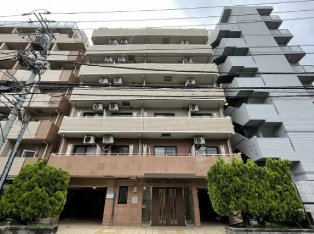 - モダンな外観のマンション、エアコンが設置されたバルコニーと緑の植栽がある玄関前の景観